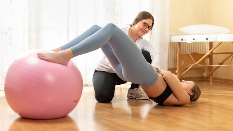 Physio talks to woman resting her feet on a fit ball