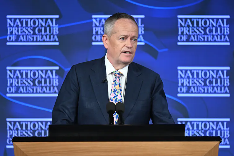 Man in a suit speaking at a lectern.
