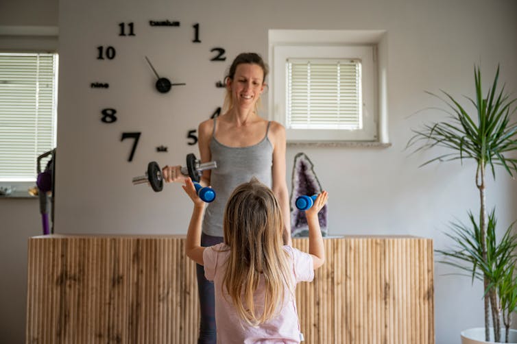 A mother and daughter lifting weights at home.
