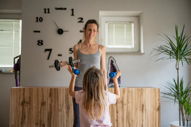 A mother and daughter lift weights at home.