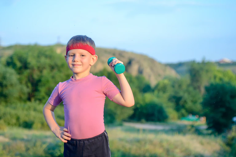 A boy lifts weights outdoors in a field.