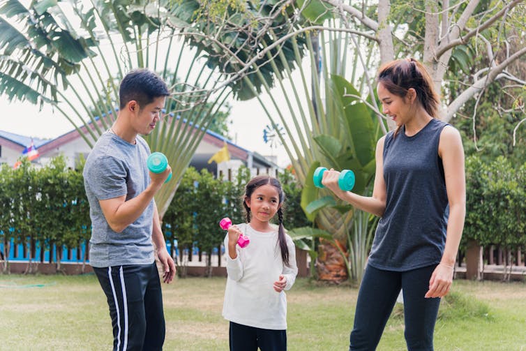 A family exercises with dumbbells in the park.
