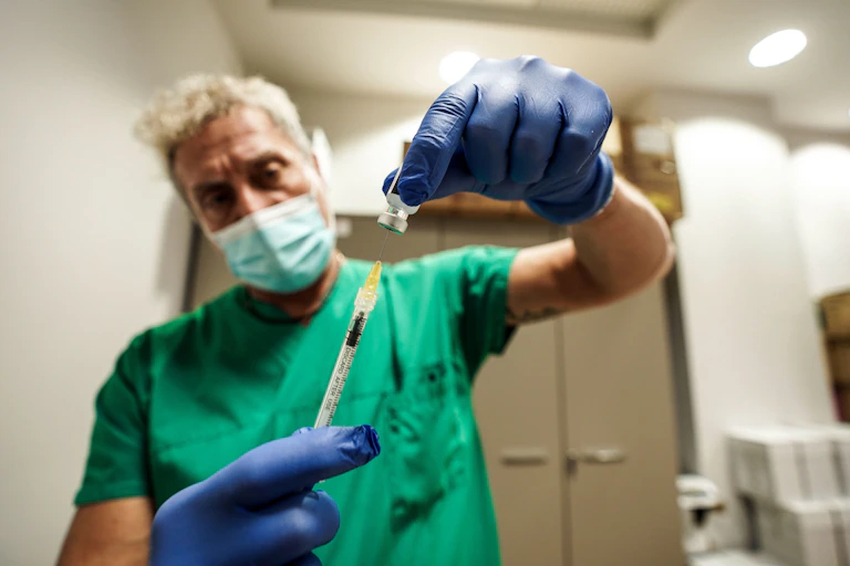 A man in green scrubs drawing up a vaccine.