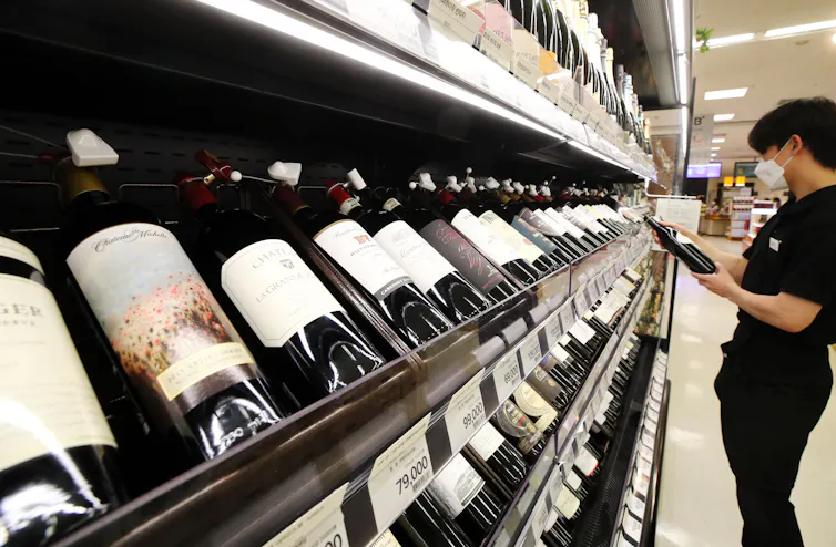 A man in South Korea choosing a bottle of wine from a supermarket shelf.