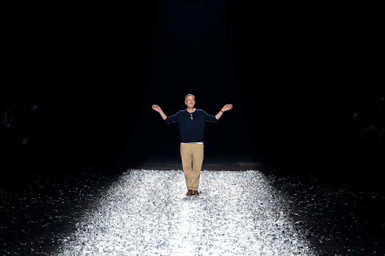 A man standing on a silver floor of a catwalk with his arms held aloft.