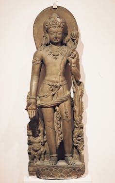 A standing statue of a God who is holding a lotus in one hand.