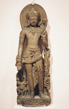 A standing statue of a God who is holding a lotus in one hand.