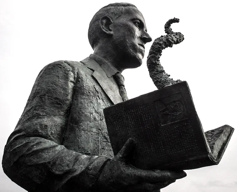 Statue of young man wearing a suit and holding an open book with a tentacle emerging from the pages of the book.