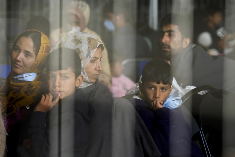 Children and women in headscarves sit on chairs.