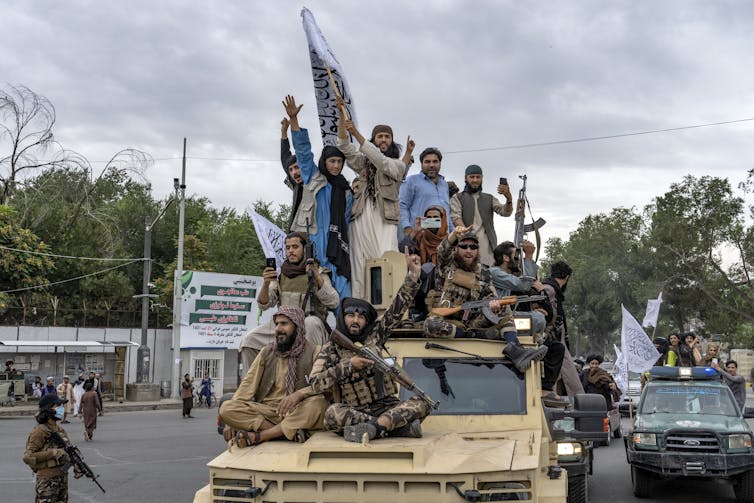 A group of men, some armed, sit on the top of a vehicle.