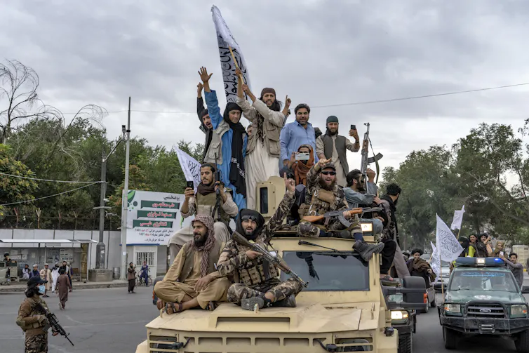 A group of men, some armed, sit on the top of a vehicle.