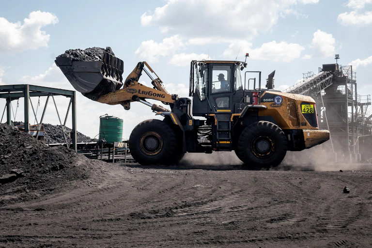 A worker driving a giant bulldozer at a coal mine, scooping up a large pile of coal