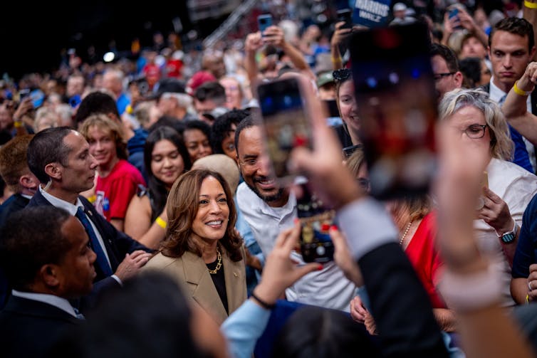 A woman stands and poses with a man, surrounded by many people in a crowd.