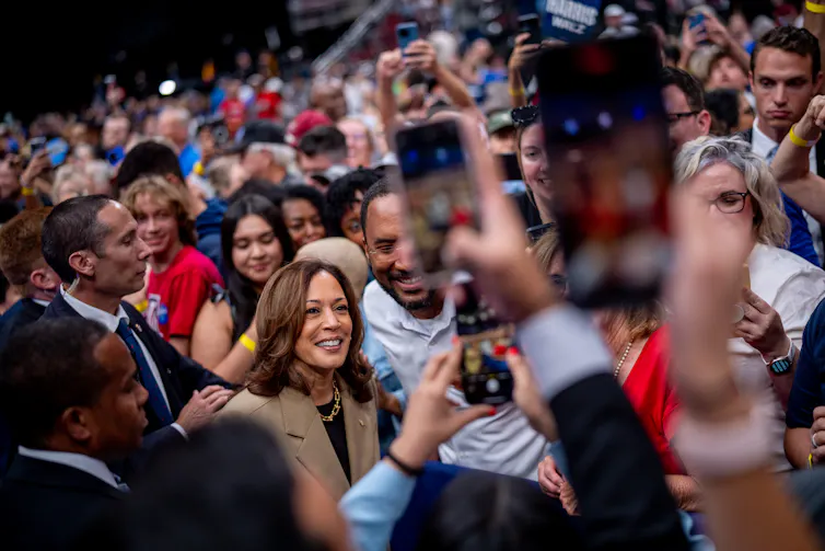 A woman stands and poses with a man, surrounded by many people in a crowd.