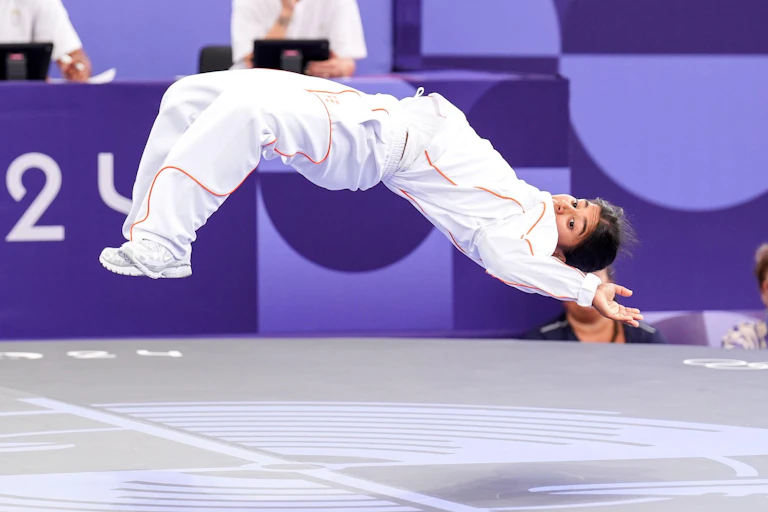 A young girl in the Olympic breakdancing competition leaps into the air.