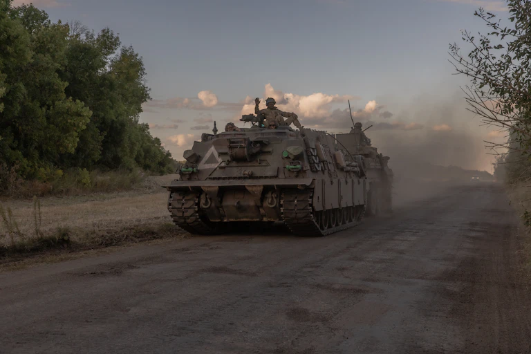 An armoured vehicle drives down a dusty track.