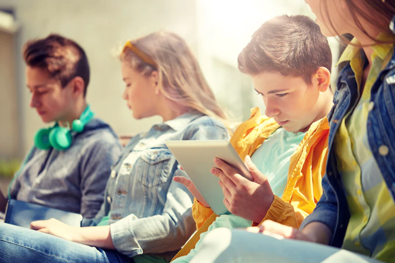 A group of teenagers use tablet computers outside