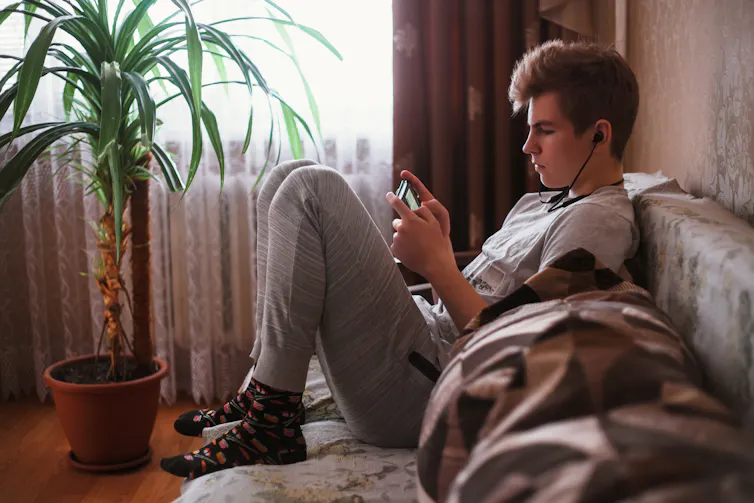 A teenager sits on a couch and watches their smartphone