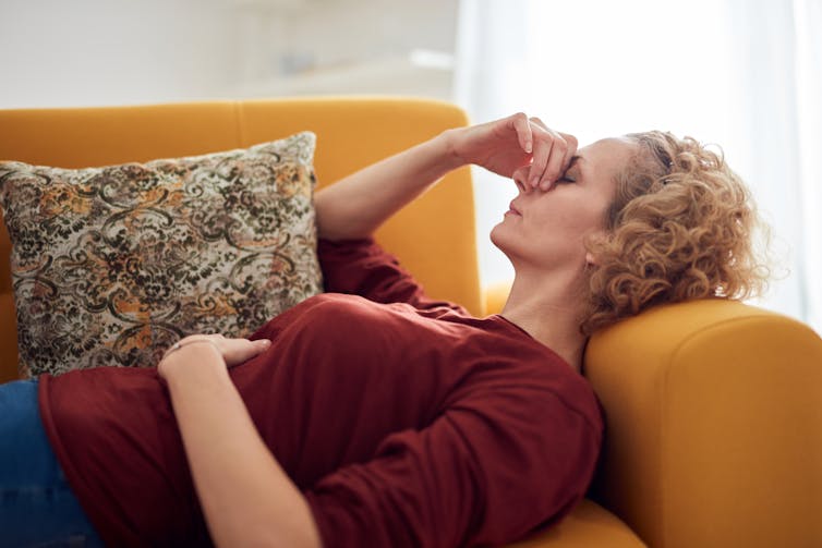 A woman lies on a couch holding her belly in pain.
