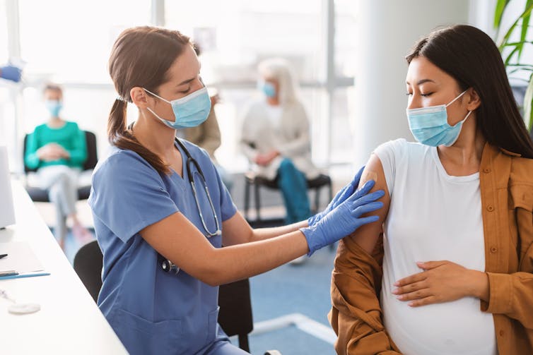 A health-care worker puts a bandaid on the upper arm of a pregnant woman.