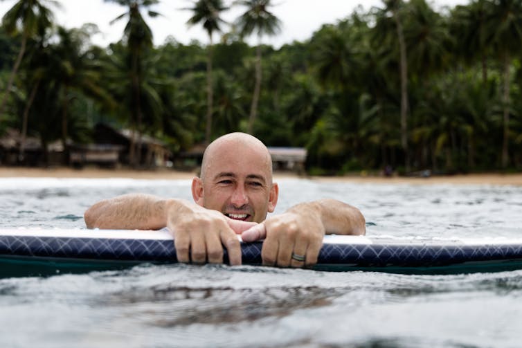 Formston in the sea, smiling and hanging onto his surfboard.