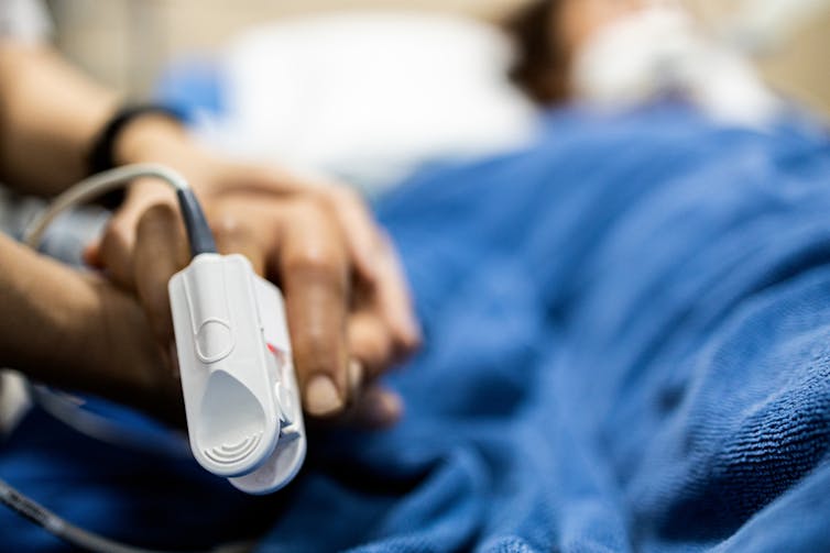 Pulse oximeter on finger of hospital patient, person holding patient's hand
