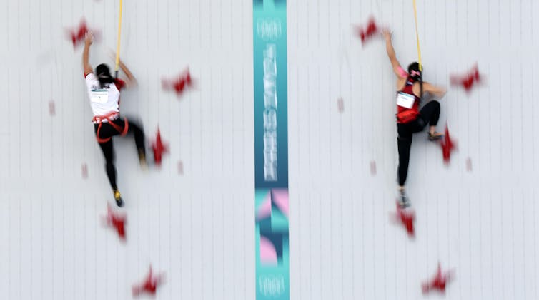 Two women speedclimbers ascending a wall at the Paris Olympics.