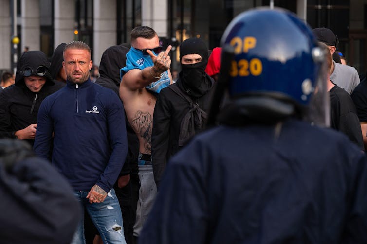 Um homem com uma camiseta cobrindo o rosto mostrando o dedo do meio para a polícia.