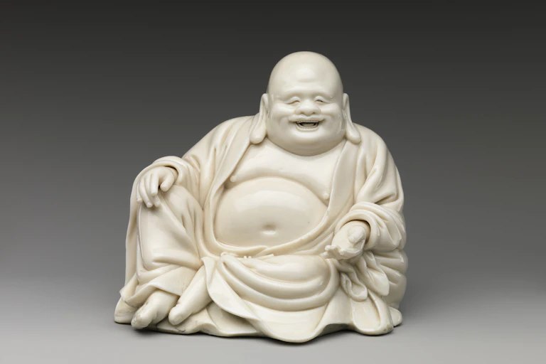 Statue of a seated Buddhist monk with a big belly and a robe draped around him.