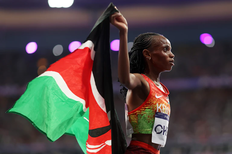 An African woman in athletics vest in profile holding a red, white, green and black flag up behind her.