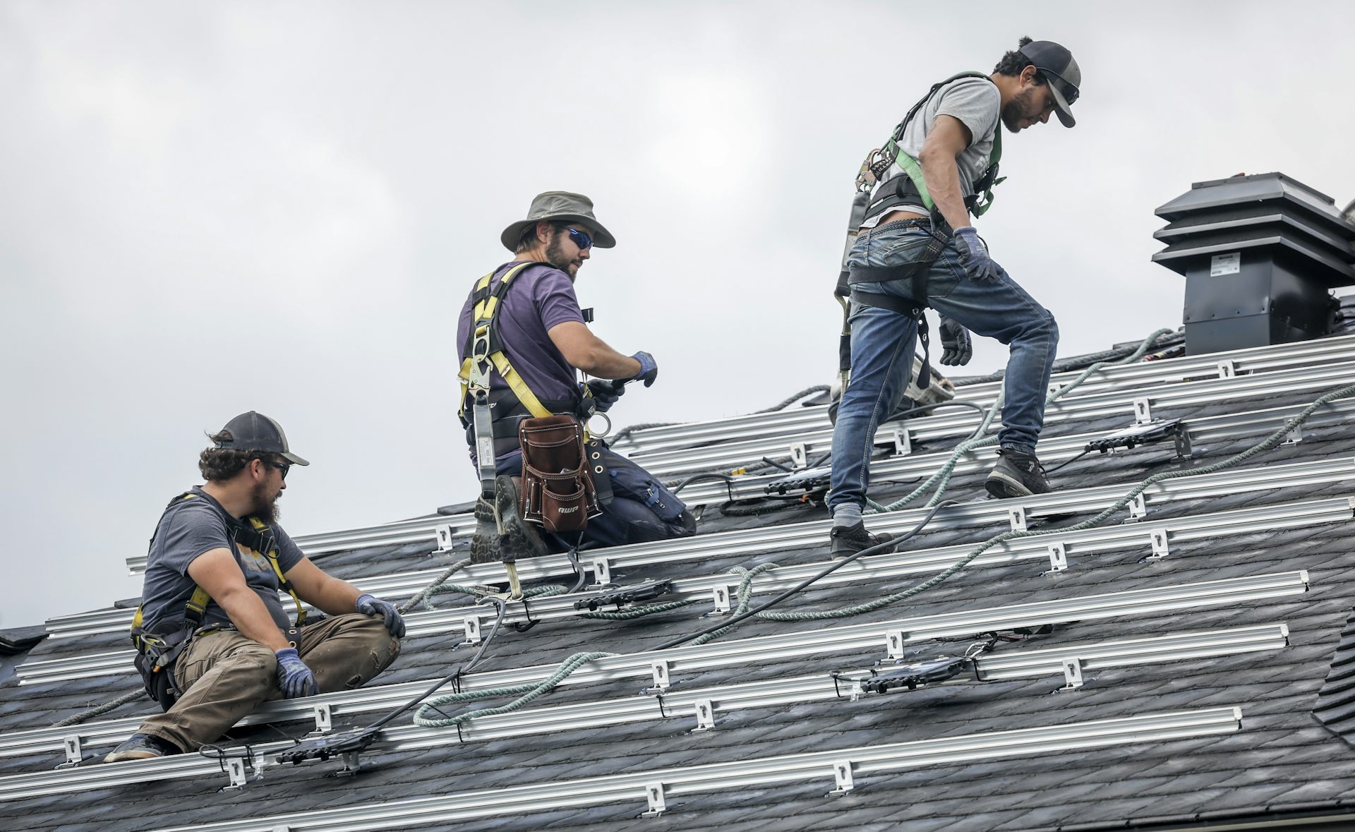 Workers stand on a roof installing solar panels.