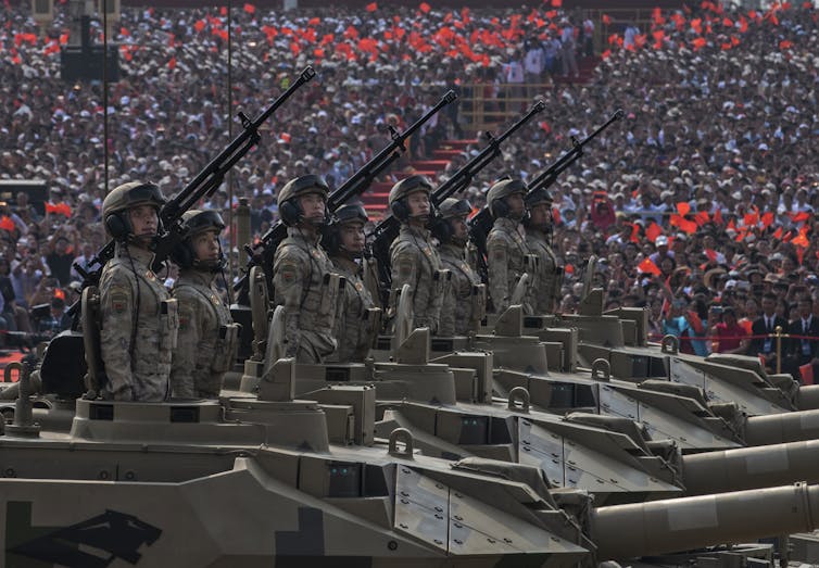 Chinese soldiers stand atop tanks in a military parade.