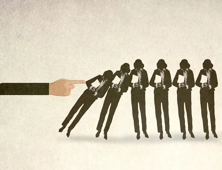 An Illustration of an oversized hand toppling a line of businesswomen.