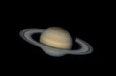 A blurry but distinct image of a pale yellow planet with oval rings around it.