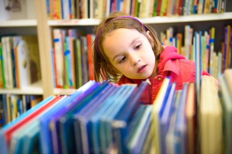 A young girl looks at books on a shelf in a library.