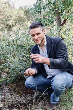 The author, Jake Robinson, crouching near the ground holding some soil while looking at the camera, smiling