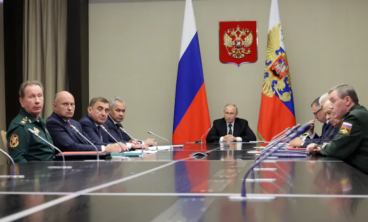 Russian president Vladimir Putin sits at the head of a long table, in between two flags and flanked by members of Russia's national security council.