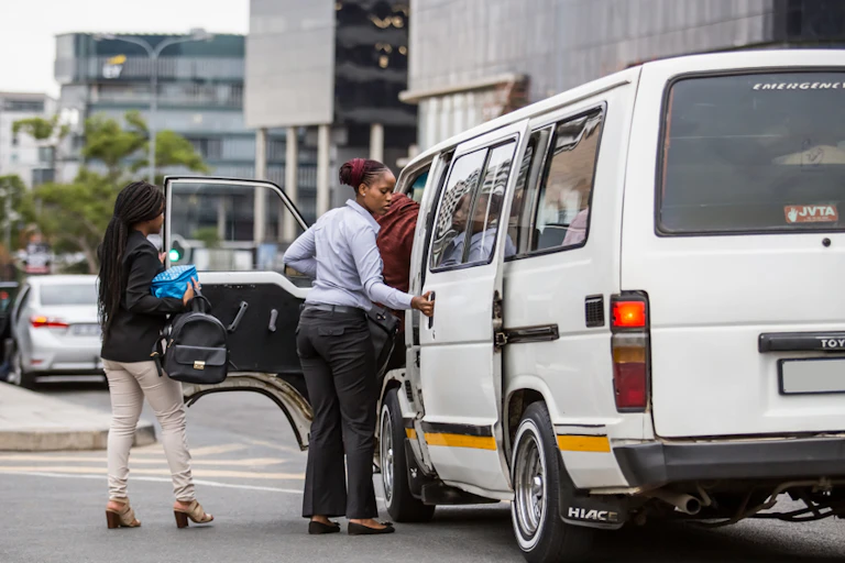 Two women approach the open doors of a stationary vehicle on a city street