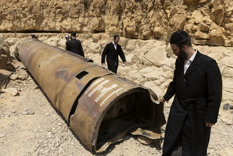 Three ultra-Orthodox men in black coats examine a huge metal rocket casing in the desert.