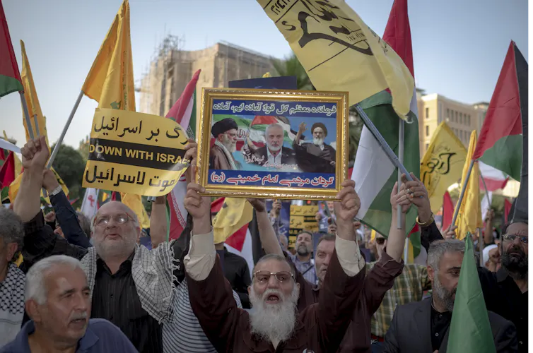 An elderly protester is holding up a framed poster featuring portraits of Iran's Supreme Leader, Ayatollah Ali Khamenei (L), Late Leader, Ayatollah Ruhollah Khomeini (R), and Hamas Leader Ismail Haniyeh,