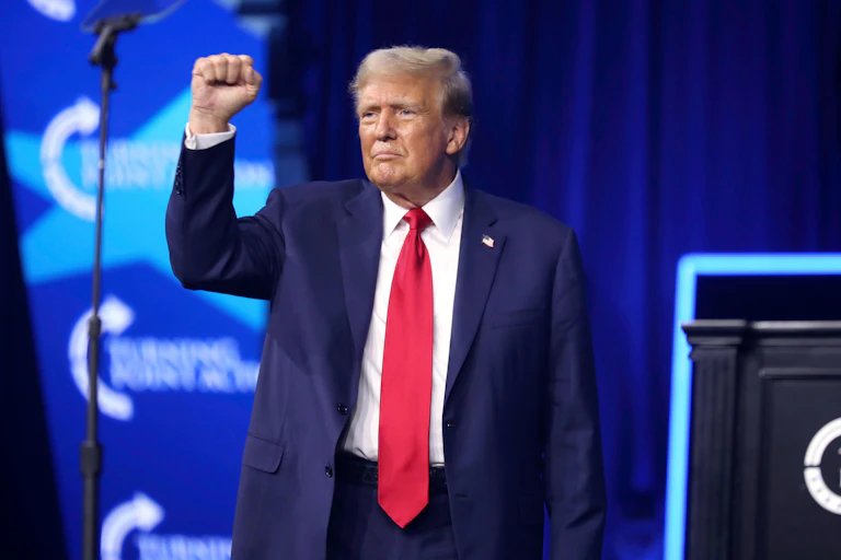 Donald Trump at a microphone with his arm raised.