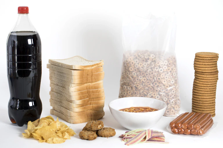 A collection of ultraprocessed foods including chips, soda, a stack of highly processed bread, crackers, hot dogs and more.