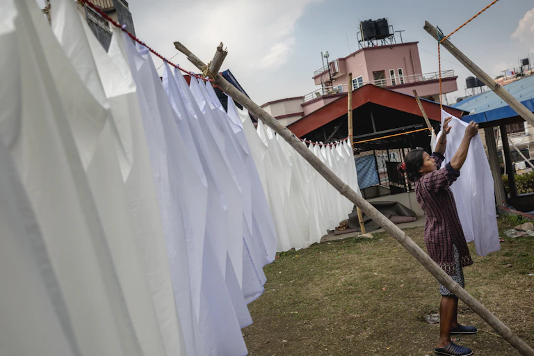 A woman is shown outside pinning a line of identical white bedsheets to a clothestring.
