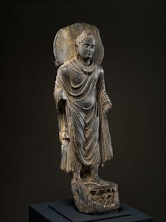 Statue of a man, with a halo around his head, wearing a robe with multiple folds.