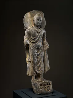 Statue of a man, with a halo around his head, wearing a robe with multiple folds.