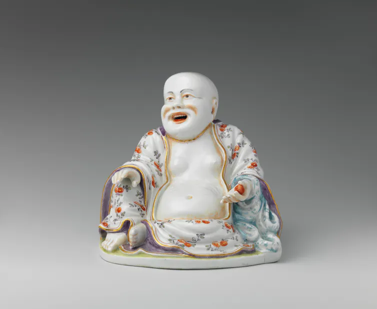 Statue of a laughing, seated monk, draped in a robe with colorful flowers.