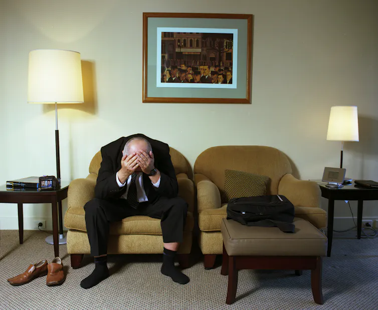 A man in a hotel, his head in his hands.