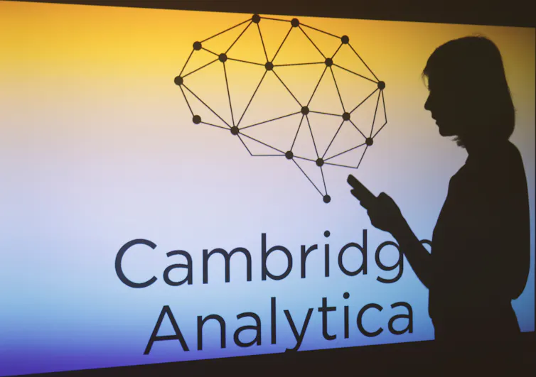 Woman walking in front of Cambridge Analytica sign as she checks a mobile device