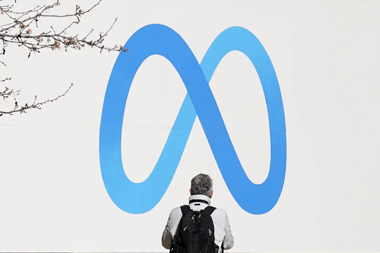 Man stands in front of blue Meta logo