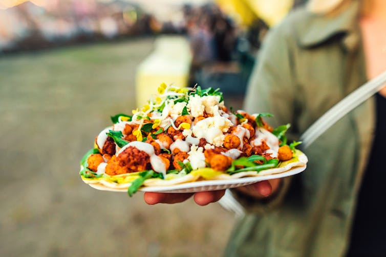A hand holding a plate filled with vegetables and pita bread.